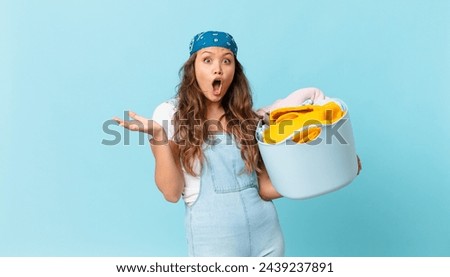 young pretty woman amazed, shocked and astonished with an unbelievable surprise and holding a wash clothes basket