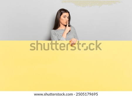young pretty woman asking for silence and quiet, gesturing with finger in front of mouth, saying shh or keeping a secret. copy space to place your concept