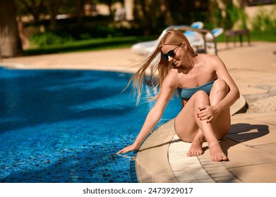 A young pretty woman with a beautiful smile in a bikini sits by the pool - Powered by Shutterstock