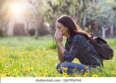 Young pretty woman blowing nose in grassland with spring flowers. Pollen allergy symptoms - Shutterstock ID 1067954744