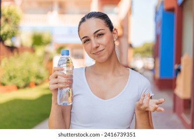 Young pretty woman with a bottle of water at outdoors making doubts gesture while lifting the shoulders - Powered by Shutterstock