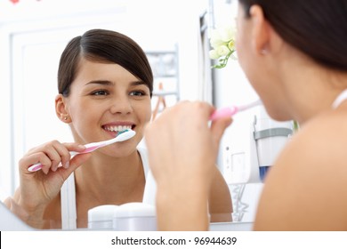 Young Pretty Woman Brushing Teeth In Front Of The Mirror