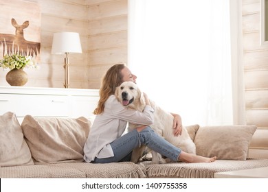 Young Pretty Woman In Casual Clothes Hugging Her Beloved Big White Dog Sitting On The Sofa In The Living Room Of Her Cozy Country House. Animal Communication Concept