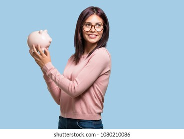 Young Pretty Woman Confident And Cheerful, Holding A Piglet Bank And Being Quiet Because The Money Is Saved, Concept Of Saving, Economy And Prosperity