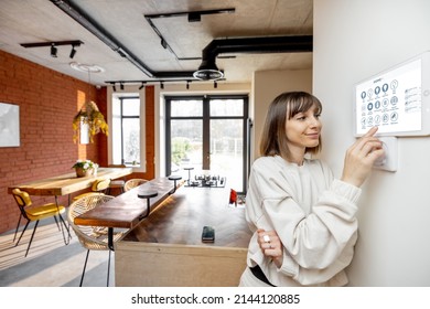 Young pretty woman controlling smart home devices with a digital tablet mounted on the wall. Wide angle view on stylish living room interior - Powered by Shutterstock