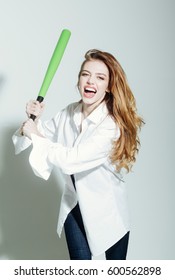 young pretty woman or cute sexy girl with beautiful long hair and red lips on adorable happy smiling face in fashionable white shirt holds green baseball bat or racket on grey background