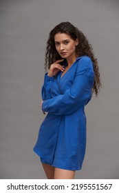 Young Pretty Woman With Dark Long Hair Looking At Camera During Fashion Photo Session In Studio While Posing Against Grey Background