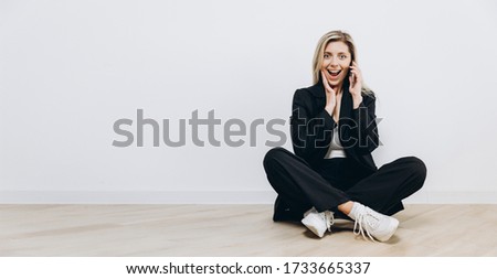 A young pretty woman dressed black is talking by mobile phone against a white background