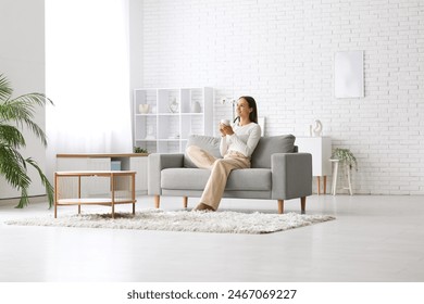 Young pretty woman drinking coffee on cozy couch at home - Powered by Shutterstock