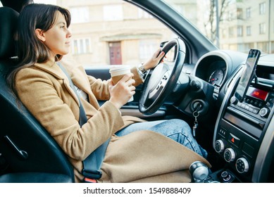 young pretty woman driving car while drinking cup of coffee