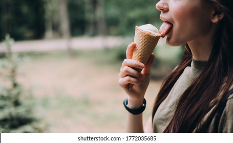 Young Pretty Woman Eating Ice Cream In A Waffle Cone While Walking Along The Street In The Park Alone.