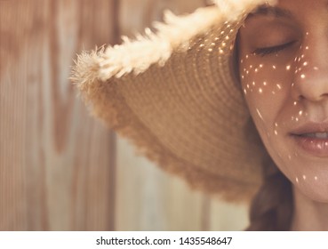 Young Pretty Woman Face Close Up And Eyes Closed With No Make Up, Sun Shadows From The Summer Hat That Looks Like Freckles On Her Face.