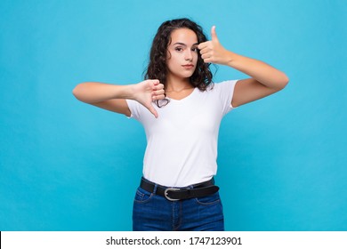 Young Pretty Woman Feeling Confused, Clueless And Unsure, Weighting The Good And Bad In Different Options Or Choices Against Blue Background