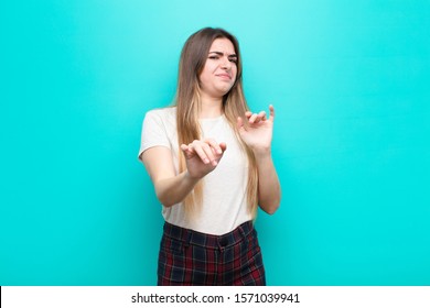 Young Pretty Woman Feeling Disgusted And Nauseous, Backing Away From Something Nasty, Smelly Or Stinky, Saying Yuck Against Blue Wall