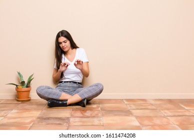 Young Pretty Woman Feeling Disgusted And Nauseous, Backing Away From Something Nasty, Smelly Or Stinky, Saying Yuck Sitting On A Floor