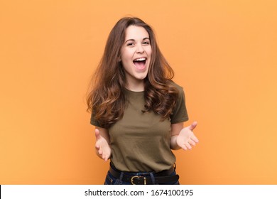 young pretty woman feeling happy, astonished, lucky and surprised, like saying omg seriously Unbelievable against orange wall