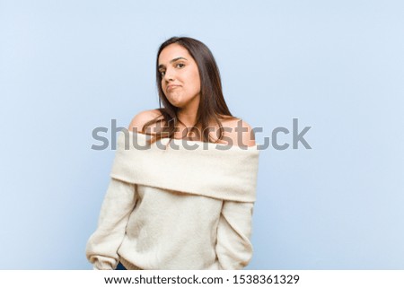 young pretty woman with a goofy, crazy, surprised expression, puffing cheeks, feeling stuffed, fat and full of food against blue background