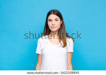 young pretty woman with a goofy, crazy, surprised expression, puffing cheeks, feeling stuffed, fat and full of food against blue wall