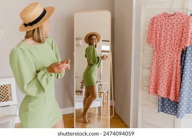 young pretty woman in green dress trying on fashion style trend dress looking in mirror at home or showroom