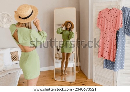 young pretty woman in green dress trying on fashion style trend dress looking in mirror at home or showroom