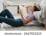 Young pretty woman with hand fan suffering from heat and lying on floor in living room