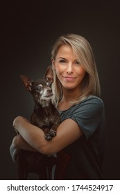 Young Pretty Woman With Her Toy Terrier Dog. Studio Shot. Moody Dark Lighting, Dark Background.