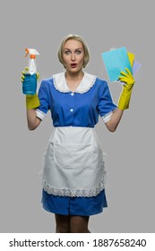 Young Pretty Woman Holding Cleaning Tools. Young Shocked House Maid Holding Cleaning Equipment And Looking At Camera.