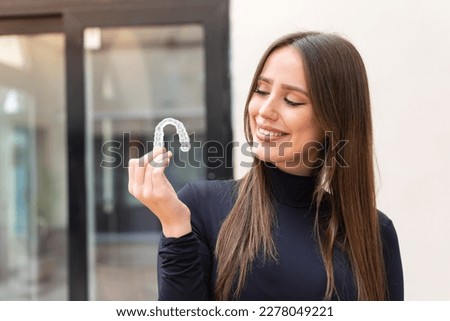 Young pretty woman holding invisible braces at outdoors with happy expression