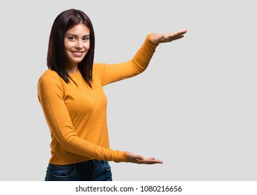 Young pretty woman holding something with hands, showing a product, smiling and cheerful, offering an imaginary object