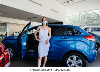 A Young Pretty Woman Inspects A New Car At A Car Dealership In A Mask During The Pandemic. The Sale And Purchase Of Cars, In The Period Of Pandemia