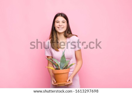 young pretty woman laughing out loud at some hilarious joke, feeling happy and cheerful, having fun with a plant