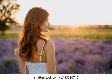Young Pretty Woman in Lavender Field Back View. Dreamy Carefree Caucasian Girl in White Dress Enjoying Sunset. Outdoors Elegant Lady Portrait on Blooming Flower Meadow Scenic Landscape