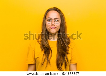 young pretty woman looking goofy and funny with a silly cross-eyed expression, joking and fooling around against orange background
