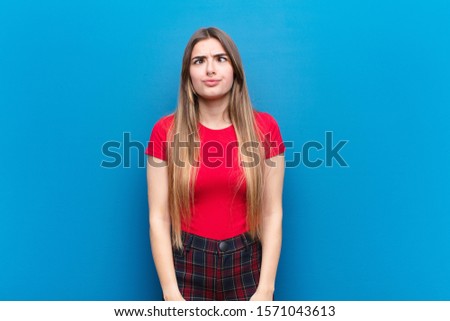 young pretty woman looking goofy and funny with a silly cross-eyed expression, joking and fooling around against blue wall