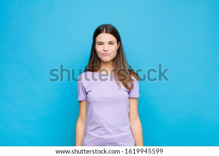 young pretty woman looking goofy and funny with a silly cross-eyed expression, joking and fooling around against blue wall