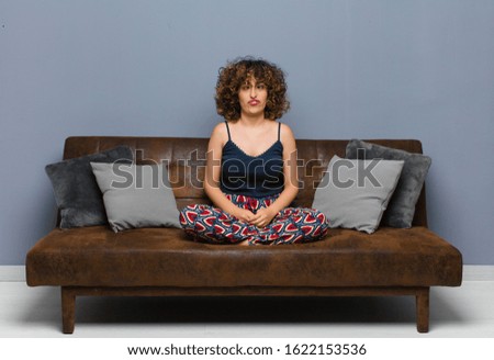 young pretty woman looking goofy and funny with a silly cross-eyed expression, joking and fooling around sitting on a sofa.