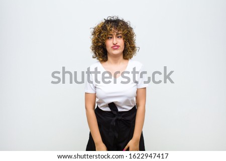young pretty woman looking goofy and funny with a silly cross-eyed expression, joking and fooling around against white wall