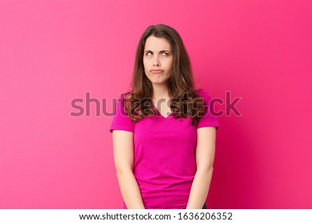young pretty woman looking goofy and funny with a silly cross-eyed expression, joking and fooling around against pink wall