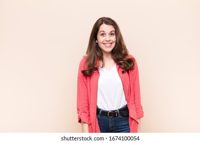 Young Pretty Woman Looking Happy And Goofy With A Broad, Fun, Loony Smile And Eyes Wide Open Against Beige Background