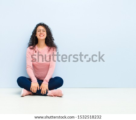 young pretty woman looking happy and goofy with a broad, fun, loony smile and eyes wide open sitting on floor