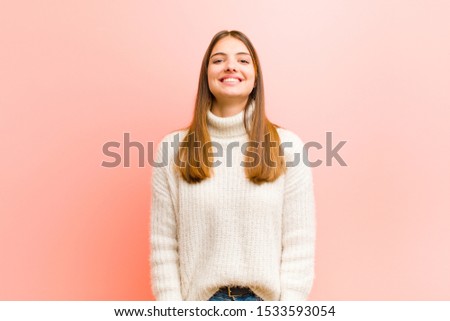 young pretty woman looking happy and goofy with a broad, fun, loony smile and eyes wide open against pink background