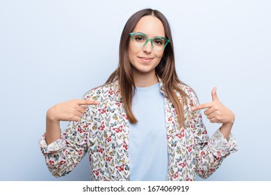 young pretty woman looking proud  positive   casual pointing to chest and both hands against blue wall