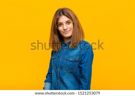 young pretty woman looking proud, confident, cool, cheeky and arrogant, smiling, feeling successful against yellow background