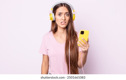 young pretty woman looking puzzled and confused. headphones and smartphone - Powered by Shutterstock