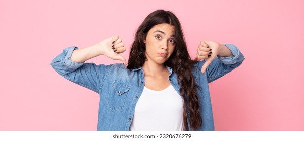 young pretty woman looking sad, disappointed or angry, showing thumbs down in disagreement, feeling frustrated - Shutterstock ID 2320676279