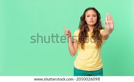young pretty woman looking serious showing open palm making stop gesture and pointing to the copy space