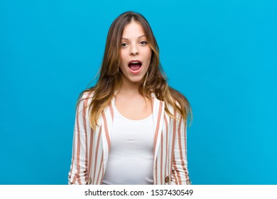 young pretty woman looking very shocked or surprised, staring with open mouth saying wow against blue wall - Shutterstock ID 1537430549