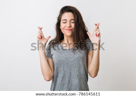 young pretty woman making a wish crossed her fingers, luck, closed eyes, hopeful gesture, isolated on white studio background