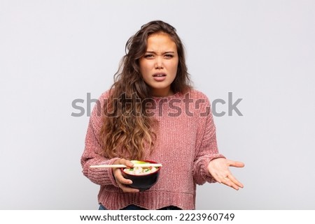 young pretty woman with noodles looking angry, annoyed and frustrated screaming wtf or what’s wrong with you