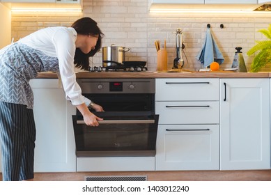 Young Pretty Woman Open Oven To Cook. Domestic Kitchen Concept. Copy Space